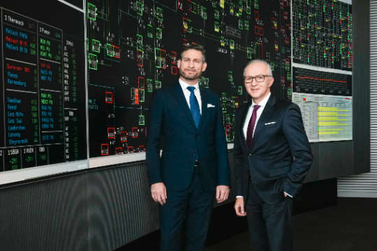 Die APG Vorstände stehen vor einer Monitorwand.