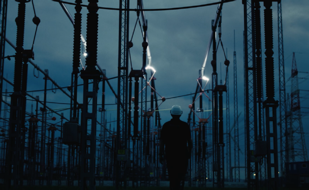 Mitarbeiter steht in Umspannwerk vor Leitungen wo elektrische Blitze bei Schaltungen entstehen.