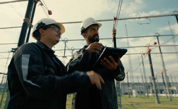 2 Mitarbeiter sprechen draussen im Umspannwerk und blicken auf ein ipad.