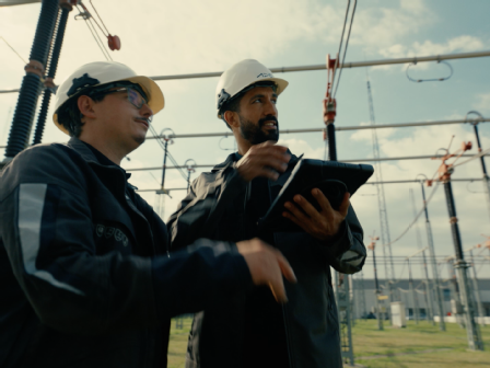 2 Mitarbeiter sprechen draussen im Umspannwerk und blicken auf ein ipad.