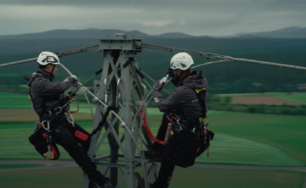 2 Freileitungstechniker führen Arbeiten auf der Spitze eines Strommasts durch.