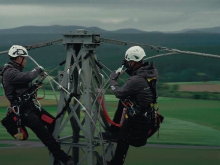 2 Freileitungstechniker führen Arbeiten auf der Spitze eines Strommasts durch.