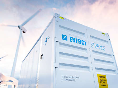 Conceptual image of a modern battery energy storage system with wind turbines and solar panel power plants in background. 3d rendering