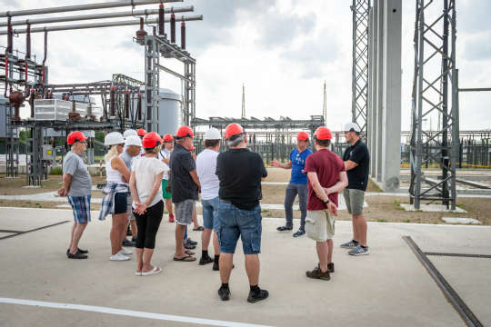 Eine Menschengruppe vor einer technischen Anlage beim Tag der offenen Türe im Umspannwerk Zaya. Eine Person präsentiert, der Rest hört zu.  Aufgenommen aus der Vogelperspektive.